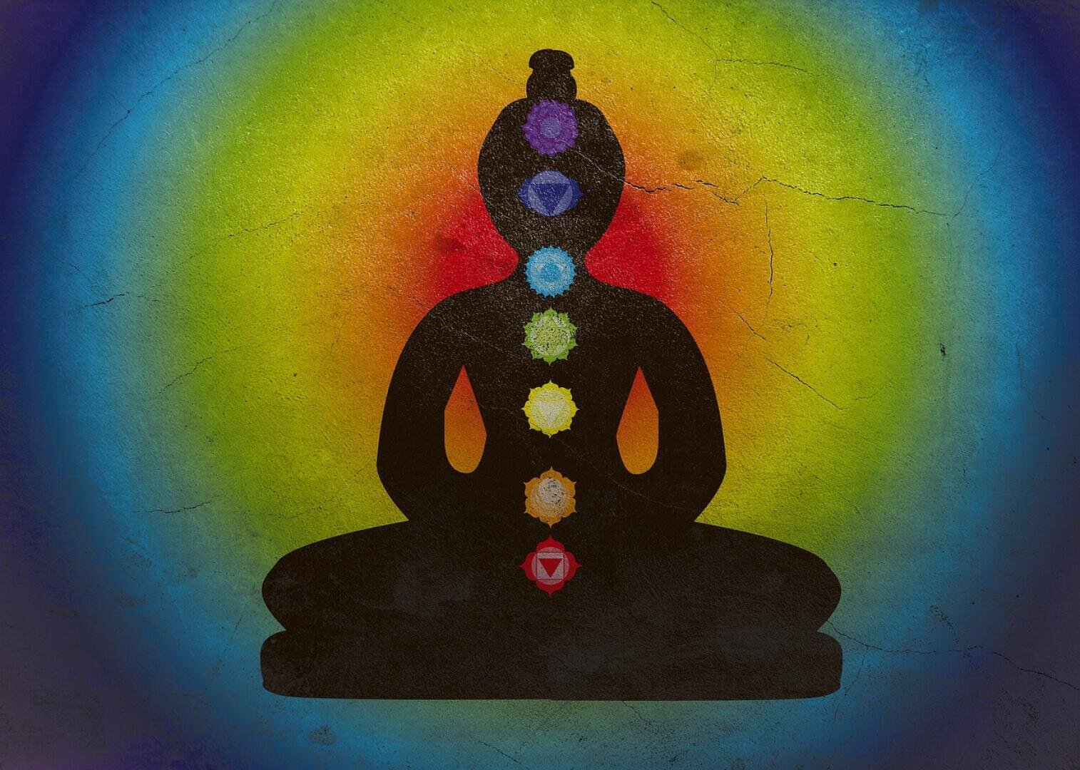 Die Silhouette einer Person, die im Lotussitz meditiert, mit sieben farbigen Chakra-Symbolen entlang der Körpermitte, vor einem leuchtenden Hintergrund mit Regenbogenverlauf.