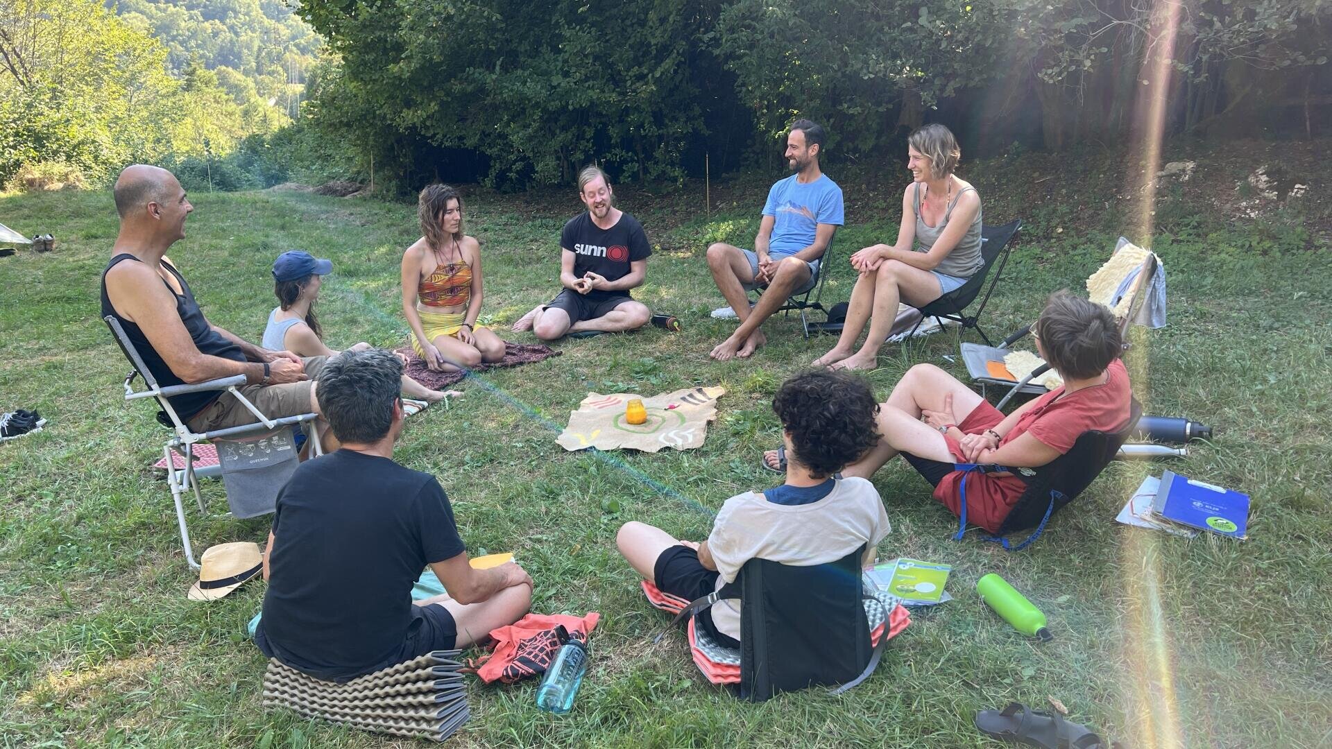 Eine Gruppe von acht Personen, die im Kreis auf einem grasbewachsenen Hügel sitzen.