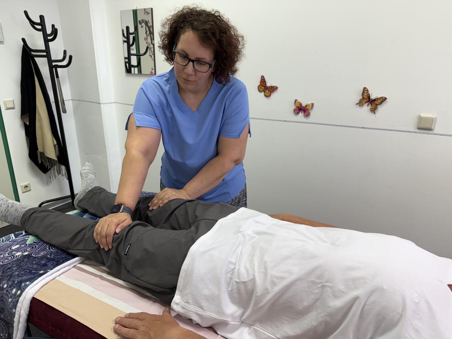 Ein Physiotherapeut in einem blauen OP-Hemd führt bei einem Patienten, der auf einer Behandlungsliege liegt, eine Beinstreckung durch.