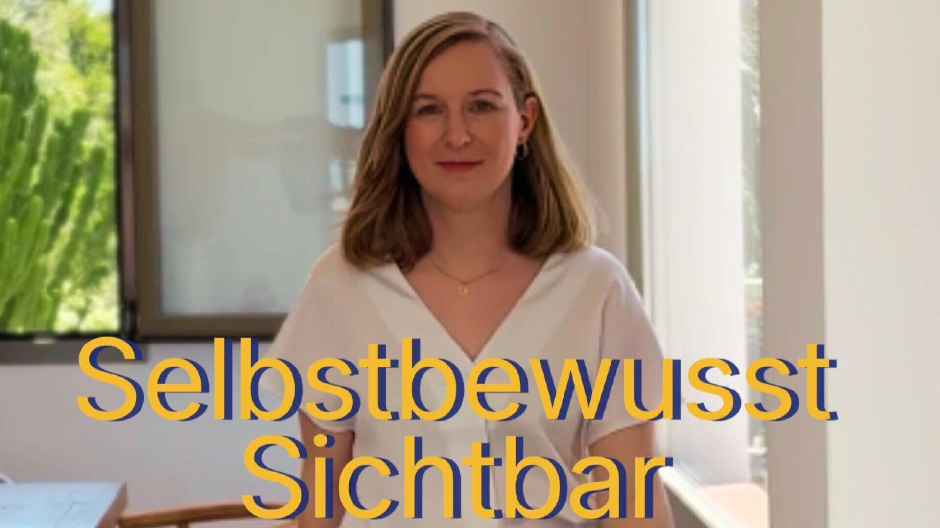 Eine Frau mit schulterlangem Haar und einem weißen Oberteil steht in einem Raum und lächelt leicht. Über dem Bild steht in großen gelben Buchstaben: „Selbstbewusst Sichtbar“. Im Hintergrund sind ein Fenster und Grünpflanzen zu sehen.