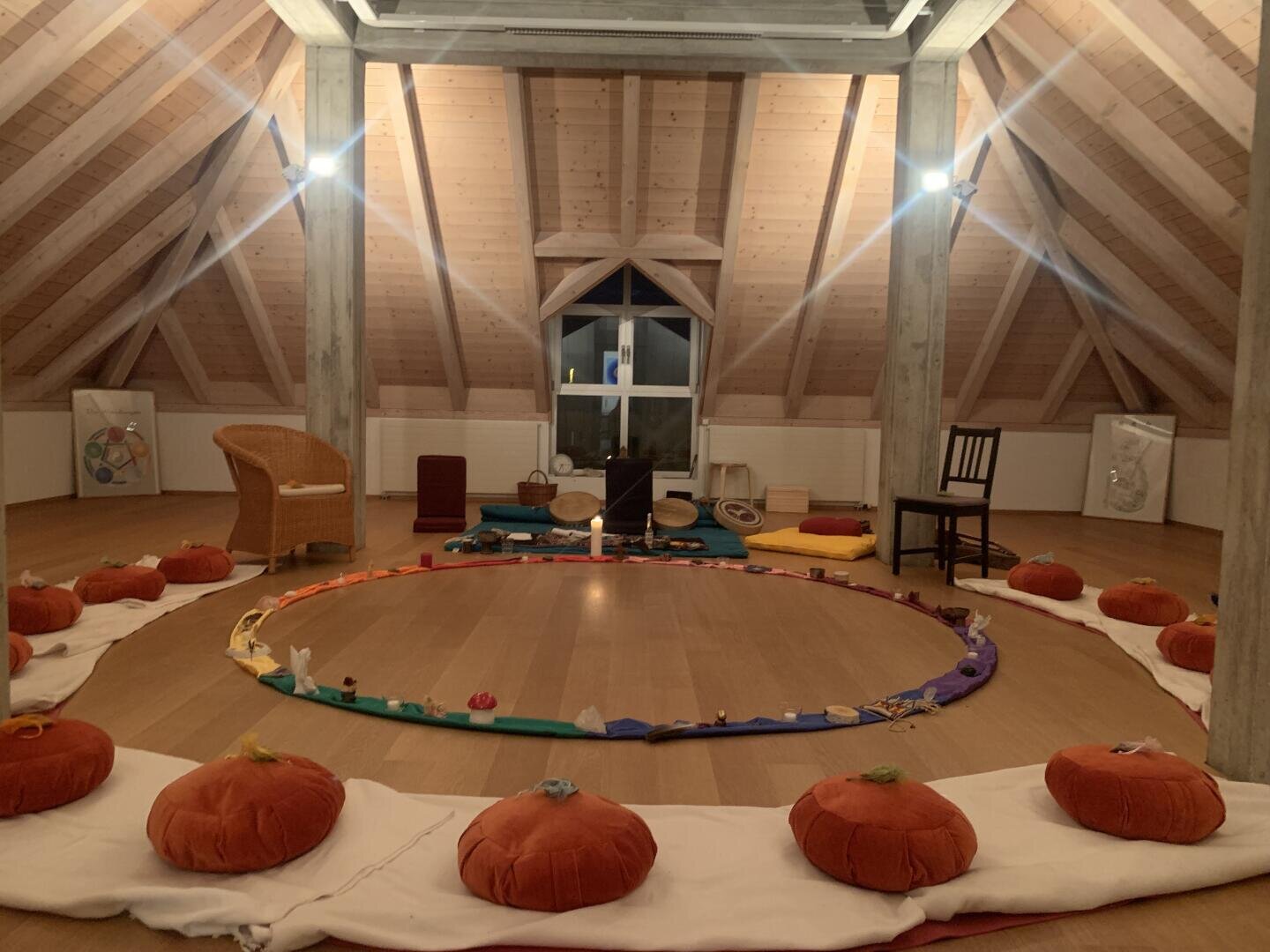 Ein Kreis aus Meditationskissen, die auf einem Holzboden in einem Dachgeschossatelier mit einem Altar in der Mitte angeordnet sind.