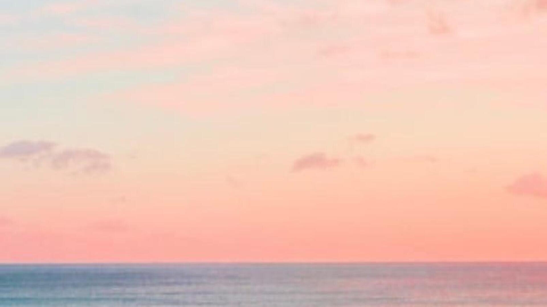 Ein ruhiger Ozean erstreckt sich unter einem pastellfarbenen Himmel mit rosafarbenen und leicht orangefarbenen Wolken, der bei Sonnenaufgang oder Sonnenuntergang eine friedliche, heitere Szene schafft.