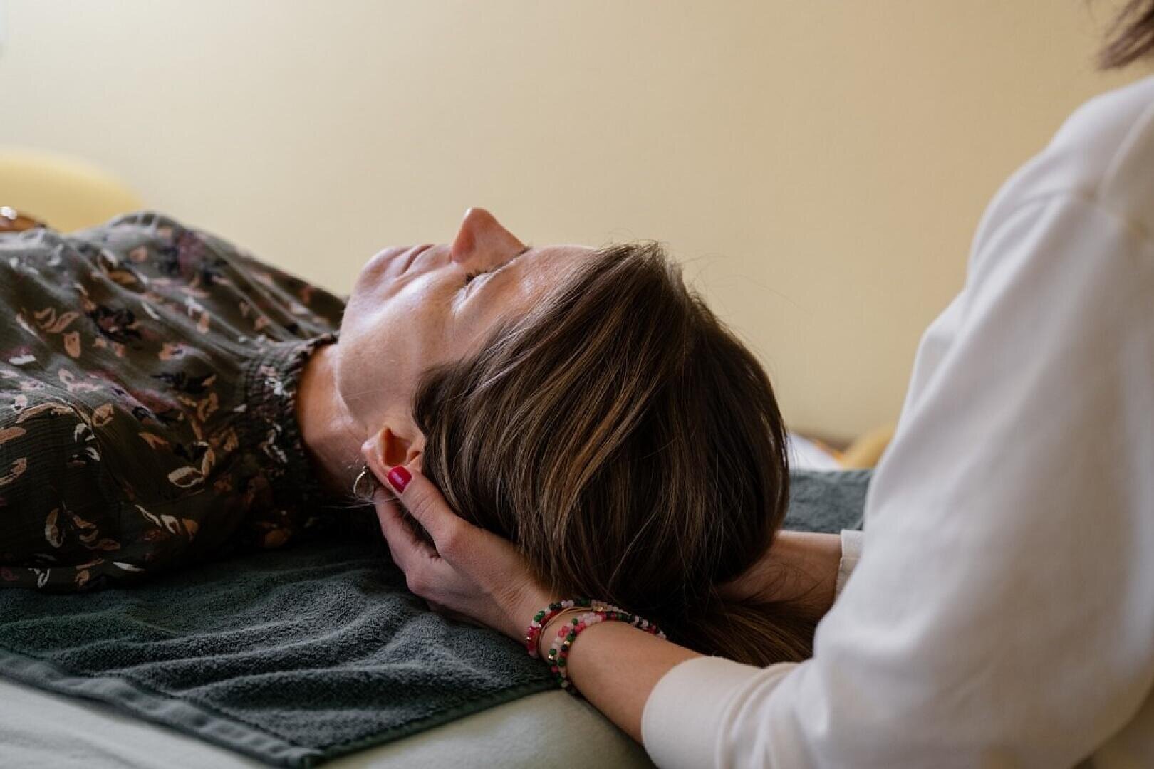 Eine Person liegt mit geschlossenen Augen da, während eine andere Person sanft ihren Kopf stützt und möglicherweise eine therapeutische oder Entspannungsbehandlung durchführt.