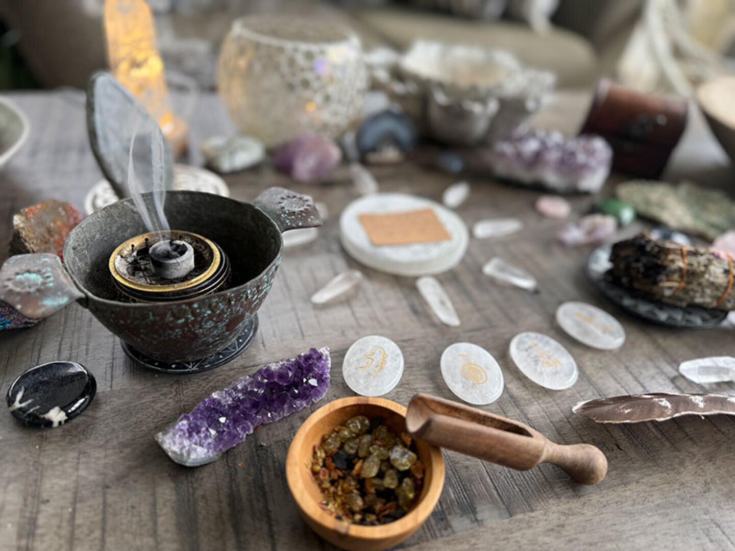 Ein Tisch mit Kristallen, in einer Metallschale brennendem Weihrauch, Runensteinen, einem Holzlöffel mit Harz und einer Feder – alles für eine spirituelle oder rituelle Atmosphäre arrangiert.