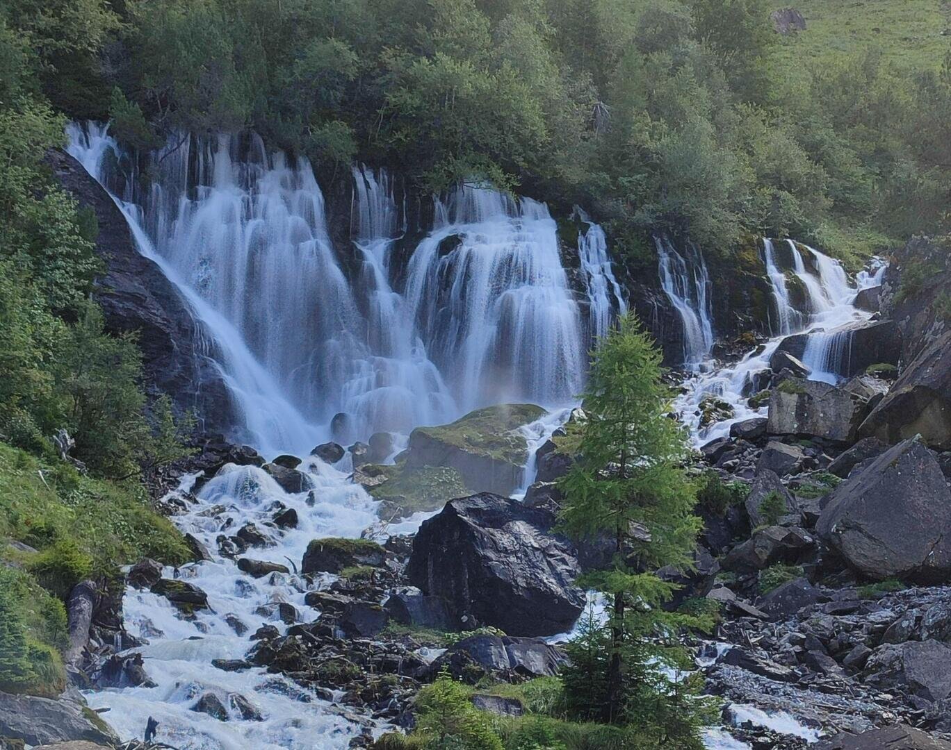 Ein breiter Wasserfall, der über felsige Klippen hinabstürzt und von Bäumen umgeben ist.