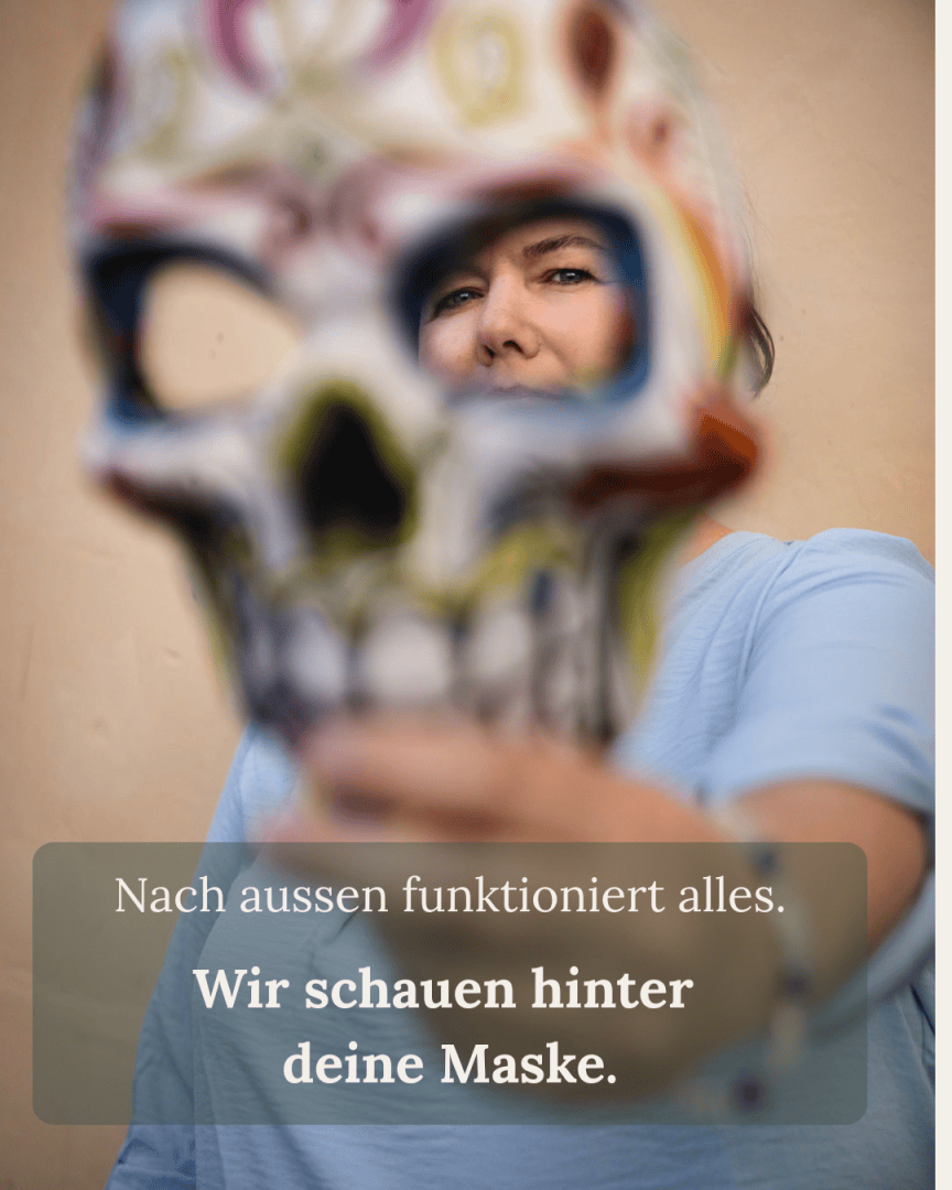 Eine Person in einem hellblauen Hemd hält eine bunte Totenkopfmaske in die Kamera, die ihr Gesicht teilweise verdeckt. Der deutsche Text lautet: Nach aussen funktioniert alles. Wir schauen hinter deine Maske.