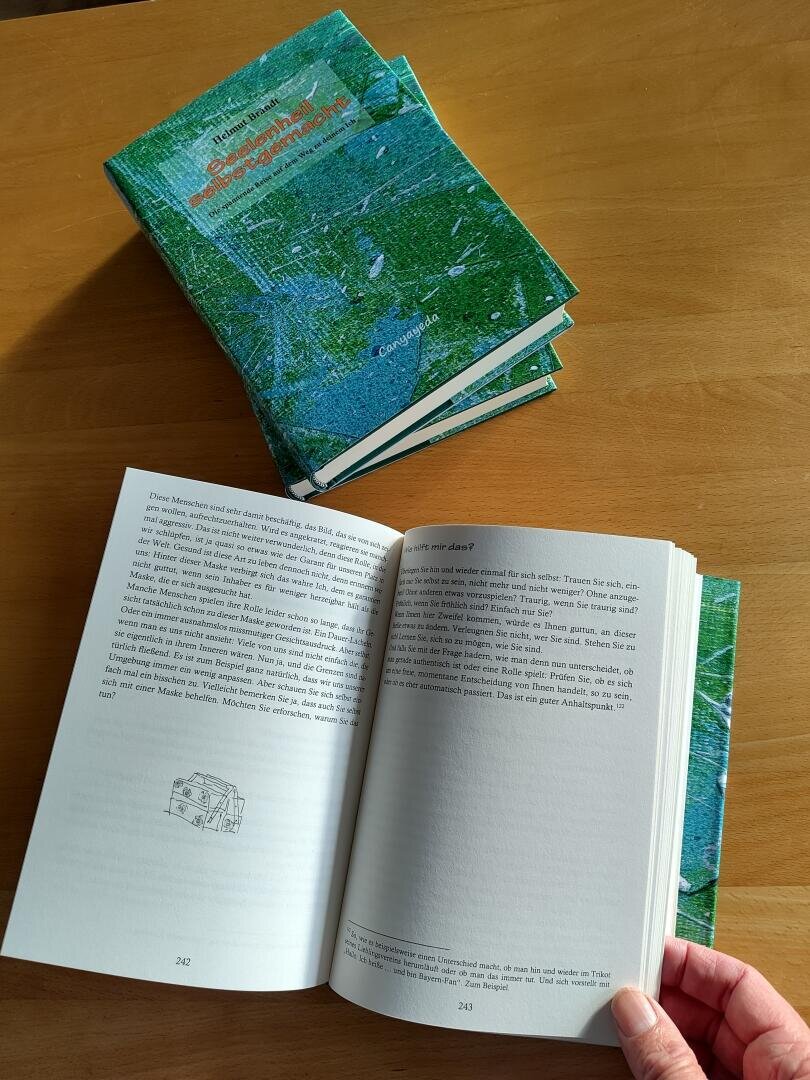 Ein offenes Buch liegt auf einem Holztisch, an dessen Oberkante ein buntes Lesezeichen steckt.