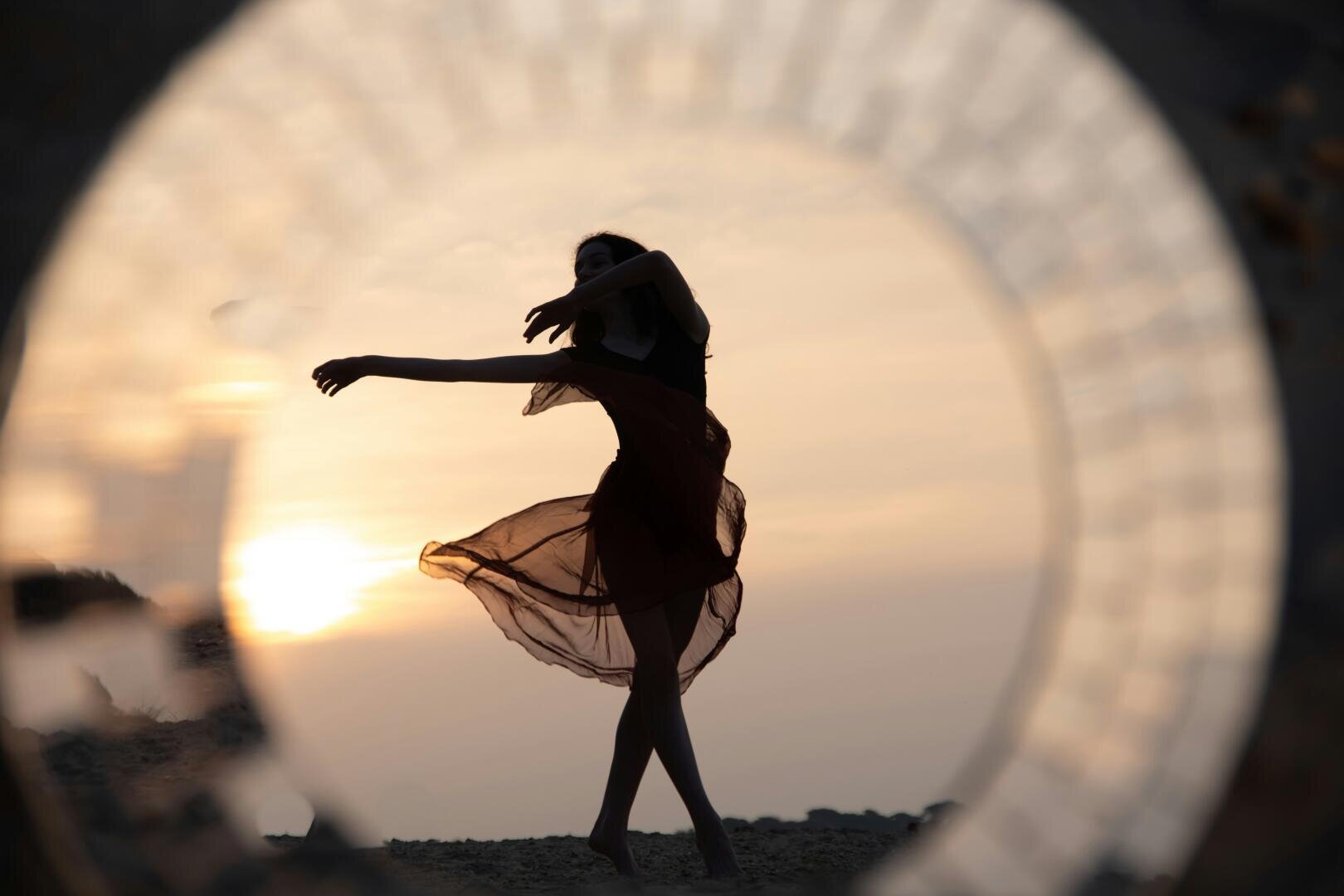 Die Silhouette einer Tänzerin, die bei Sonnenuntergang posiert, betrachtet durch einen runden Rahmen.