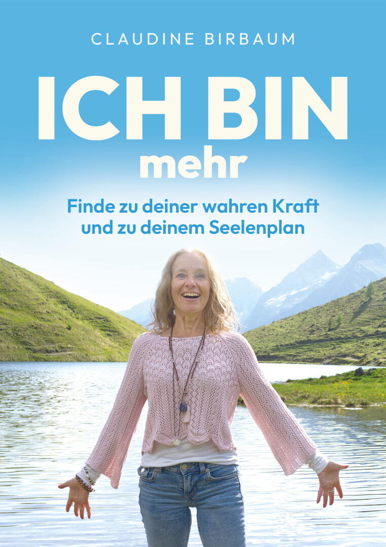 Eine lächelnde Frau steht mit ausgebreiteten Armen an einem See, im Hintergrund sind Berge und ein blauer Himmel zu sehen. Auf dem deutschen Buchcover steht: „ICH BIN mehr – Finde zu deiner wahren Kraft und zu deinem Seelenplan“ von Claudine Birbaum.