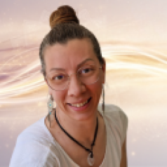 Eine Frau mit hochgestecktem Haar, die eine Brille trägt und ein weißes Hemd anhat, lächelt in die Kamera.